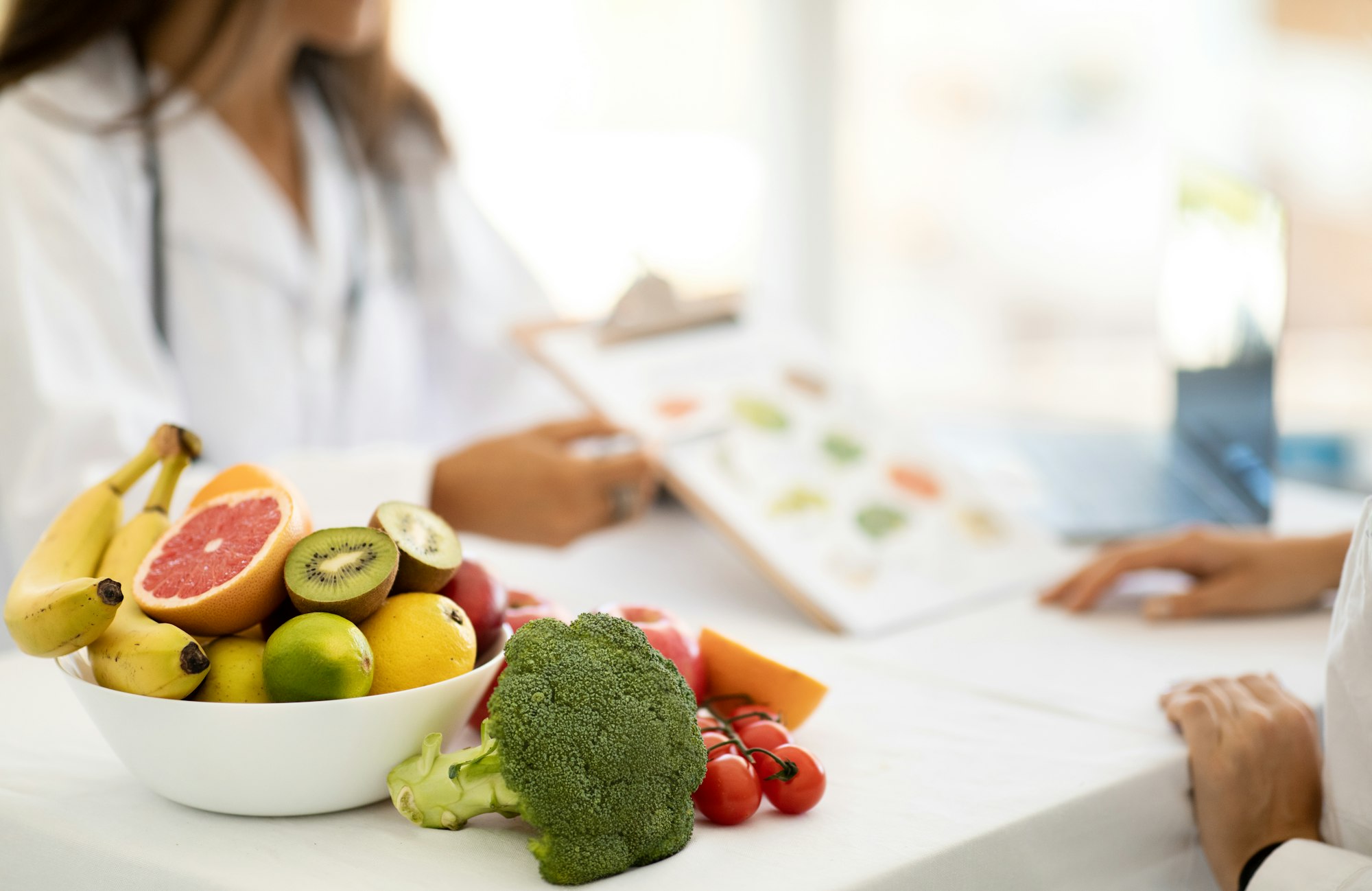 Mature caucasian doctor nutritionist in white coat recommends to young woman diet plan at table with